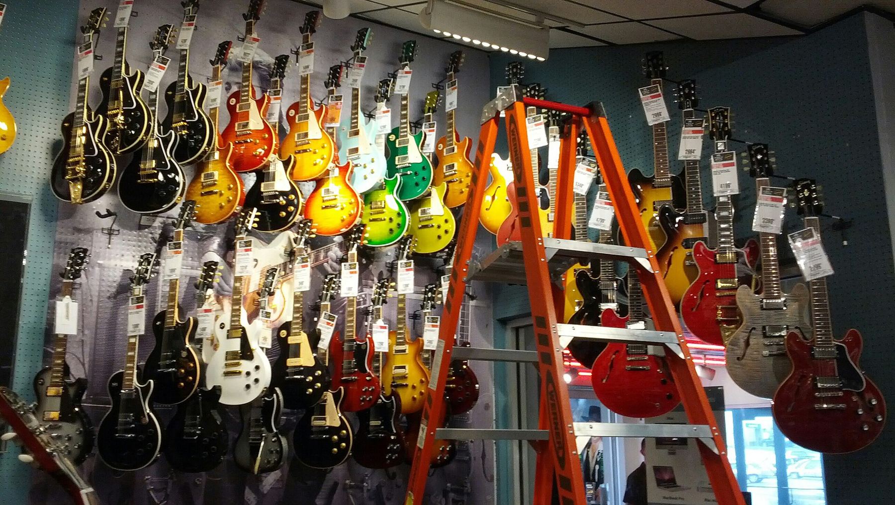 A music shop wall lined with colourful electric guitars and a tall orange ladder