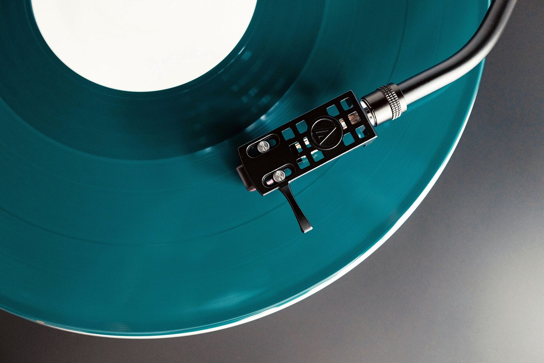 A teal vinyl record spinning on a turntable with the tonearm lowered