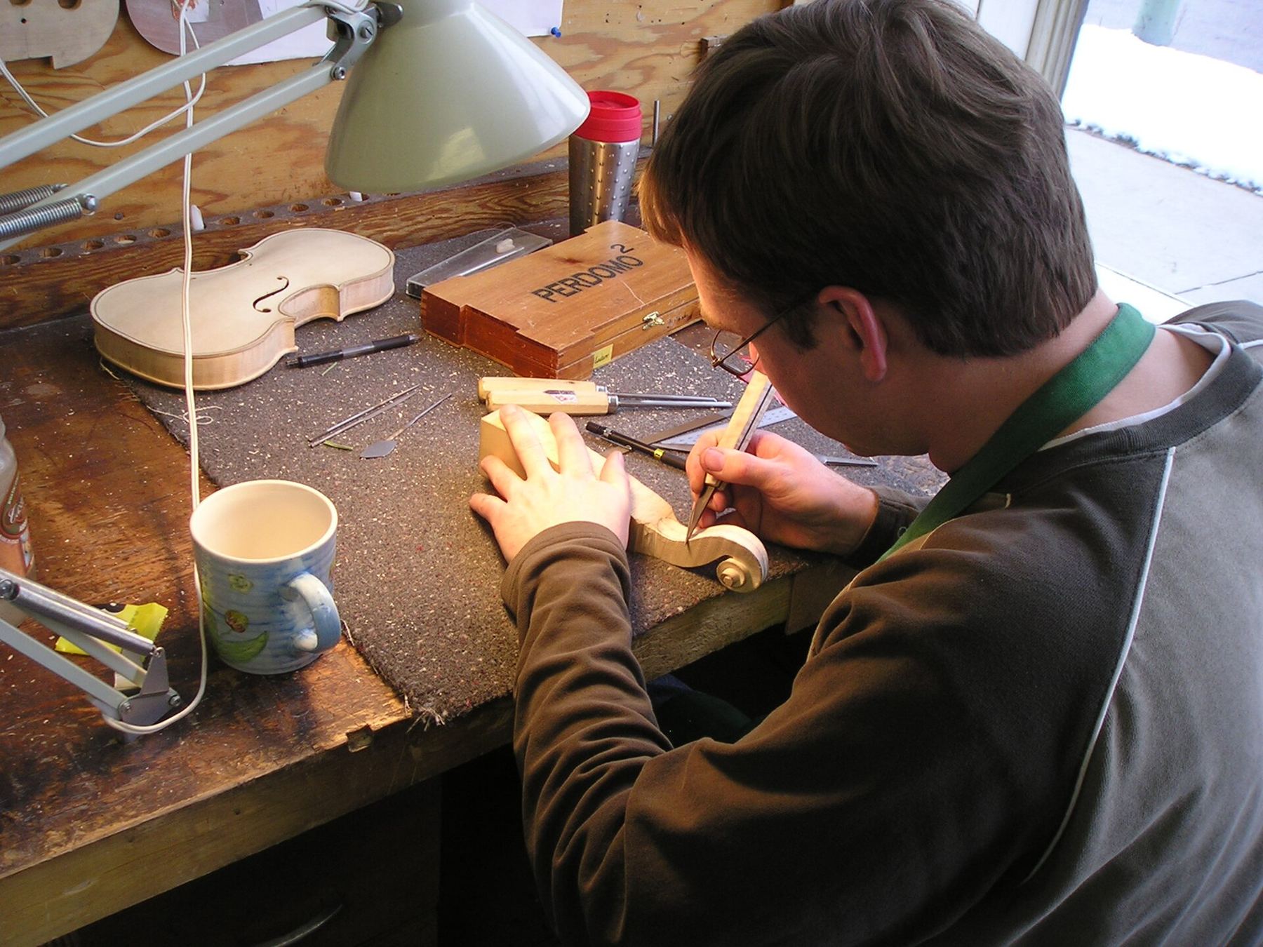 A young man carving a wooden instrument part at a workbench