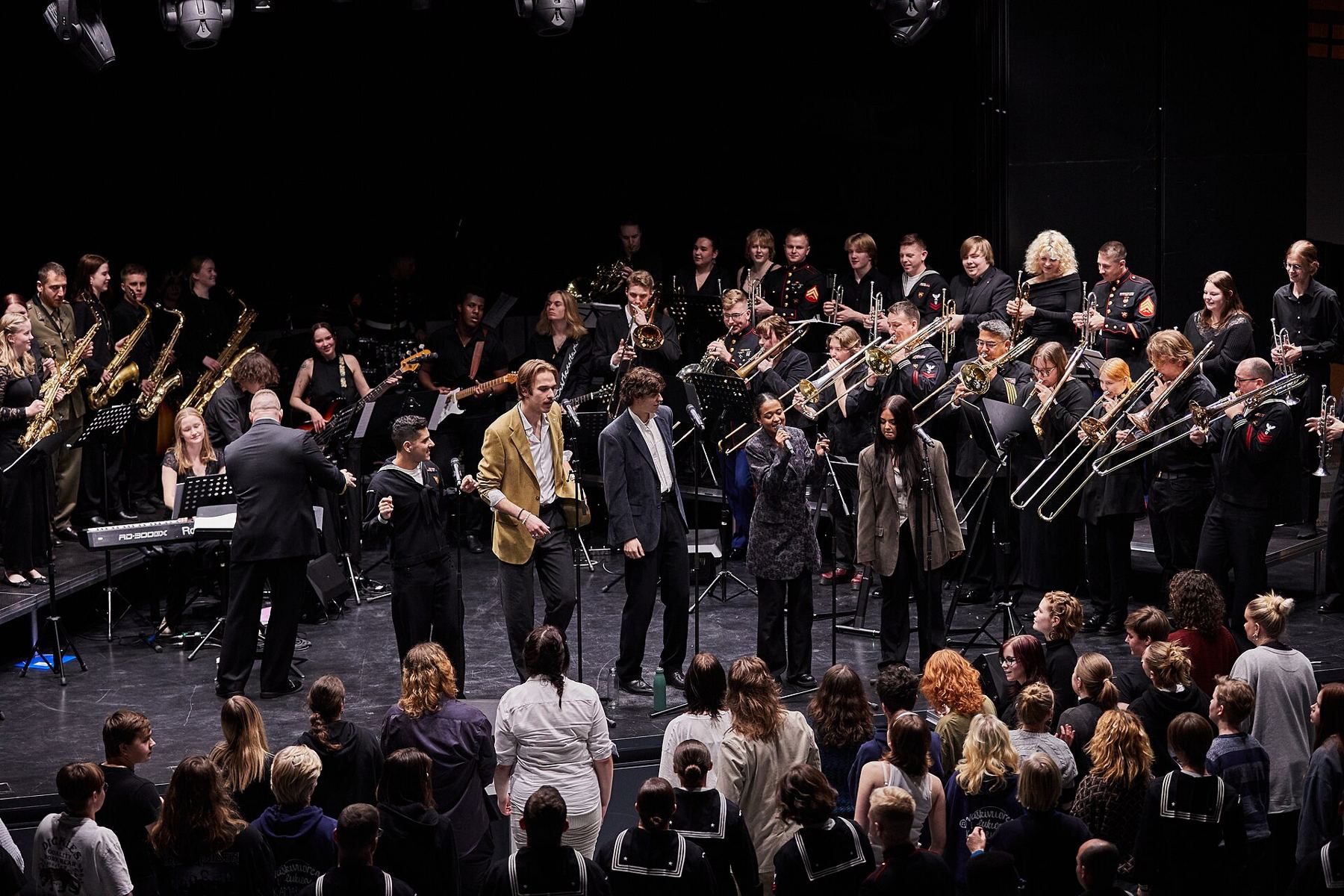 A large student ensemble performing on stage in front of an audience