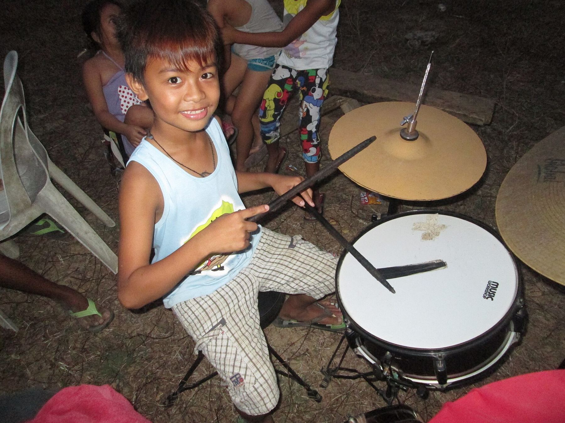 A smiling boy playing a drum kit with sticks raised