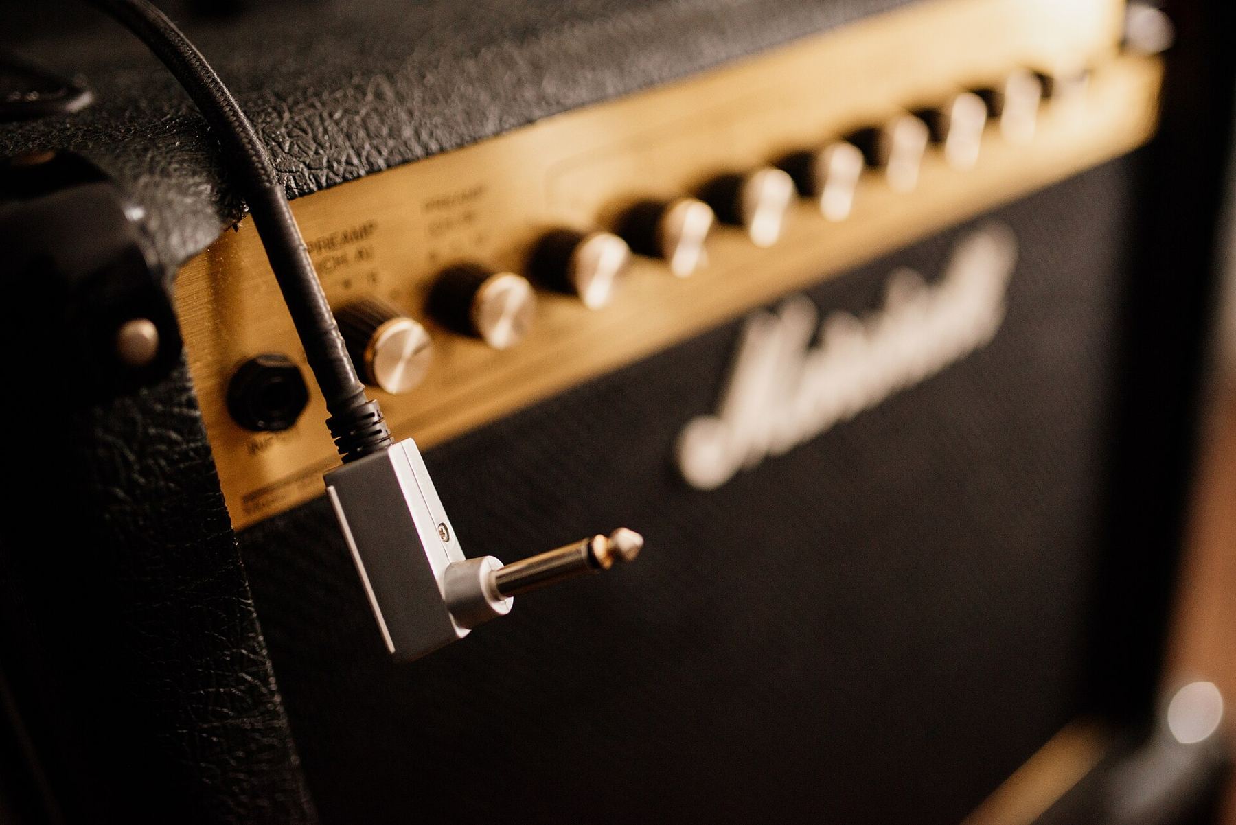 A guitar amplifier control panel with a cable plugged into the input