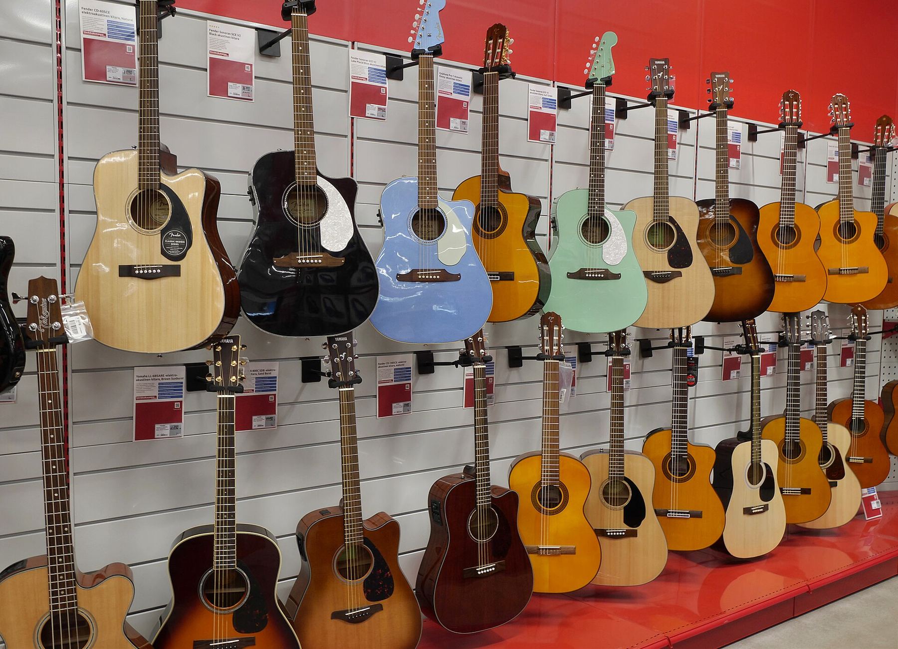 A red display wall lined with acoustic guitars in many colours