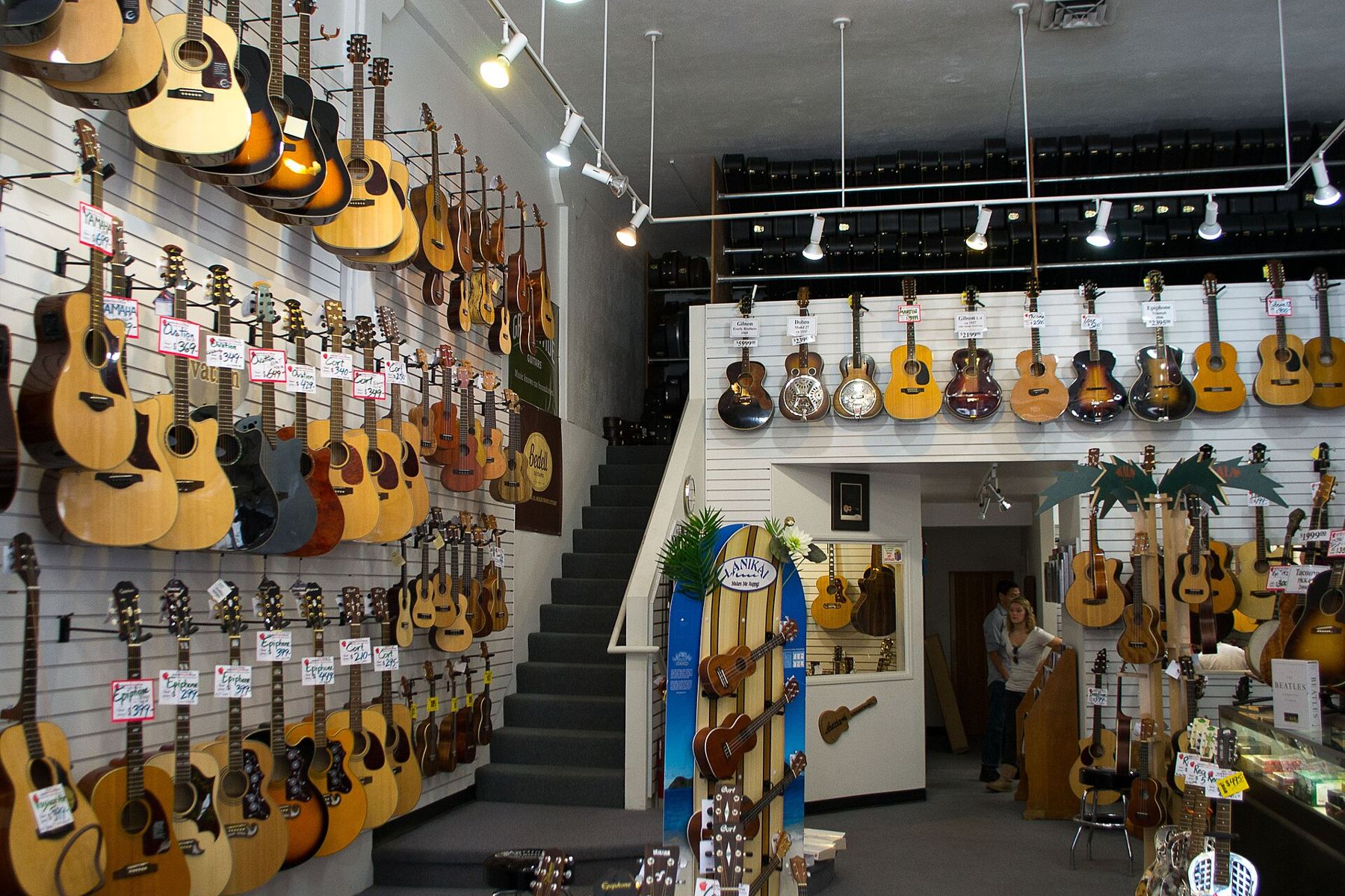 Inside a music shop with acoustic guitars hanging along two walls and a staircase