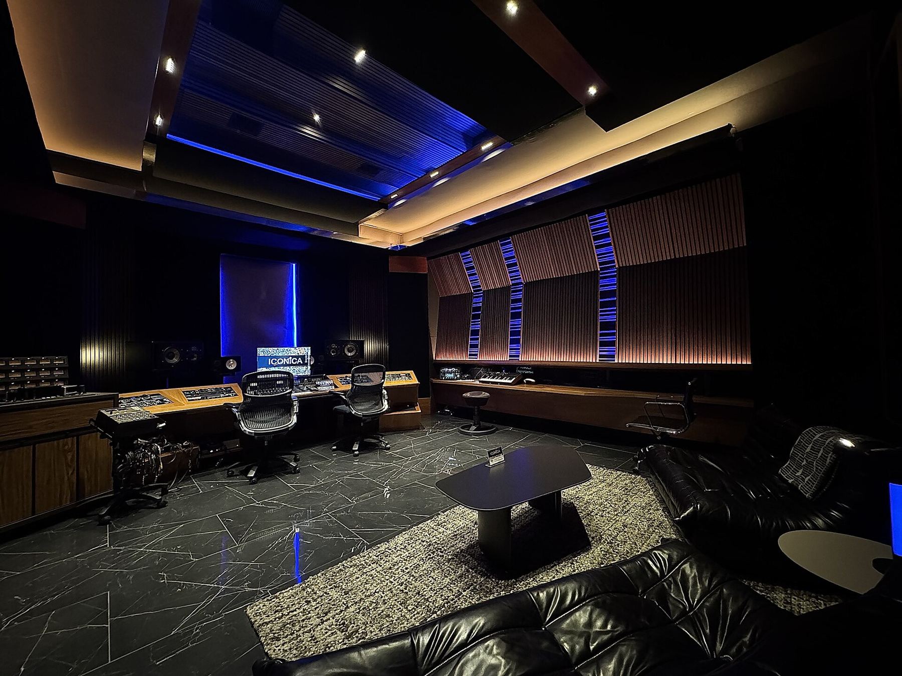 A spacious recording control room with a large mixing console and blue lighting