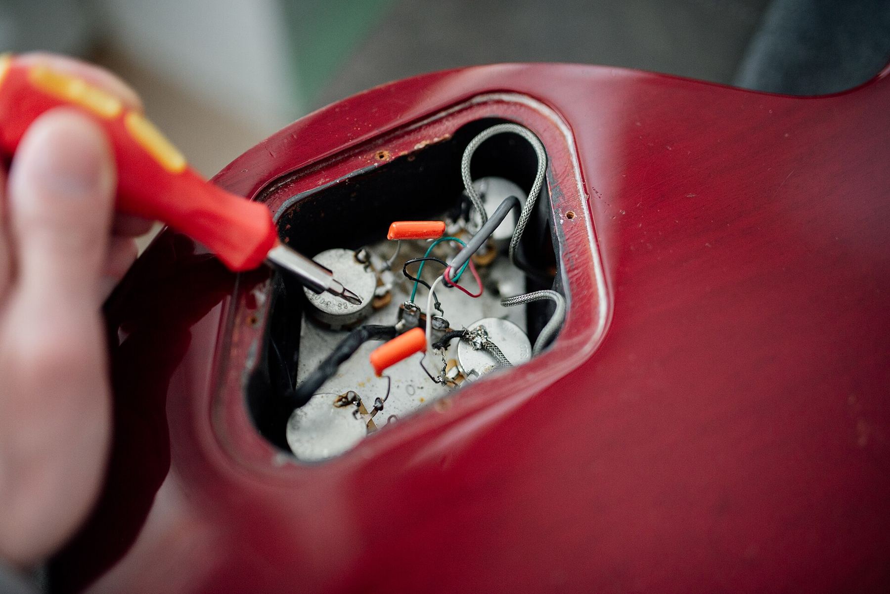 A technician soldering the wiring inside a red electric guitar