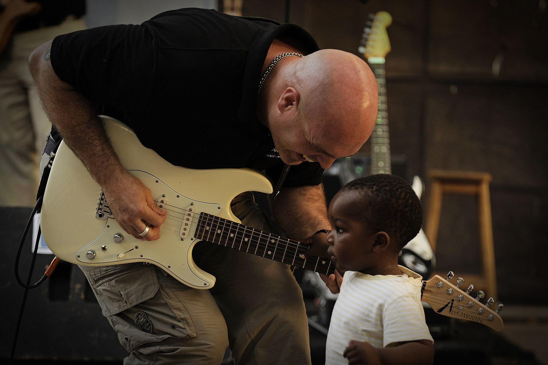 A teacher leaning in to help a young student play an electric guitar