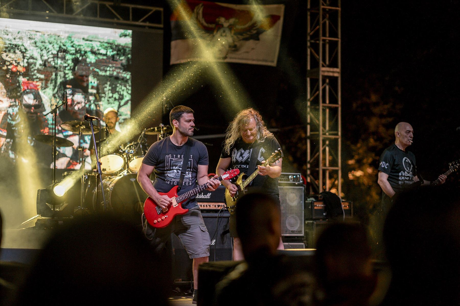 A rock band performing on a small outdoor stage under lights