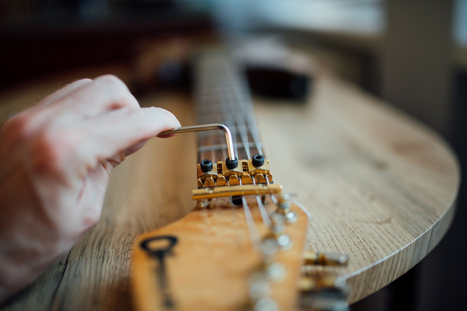 A technician's hand adjusting the bridge saddles of an electric guitar