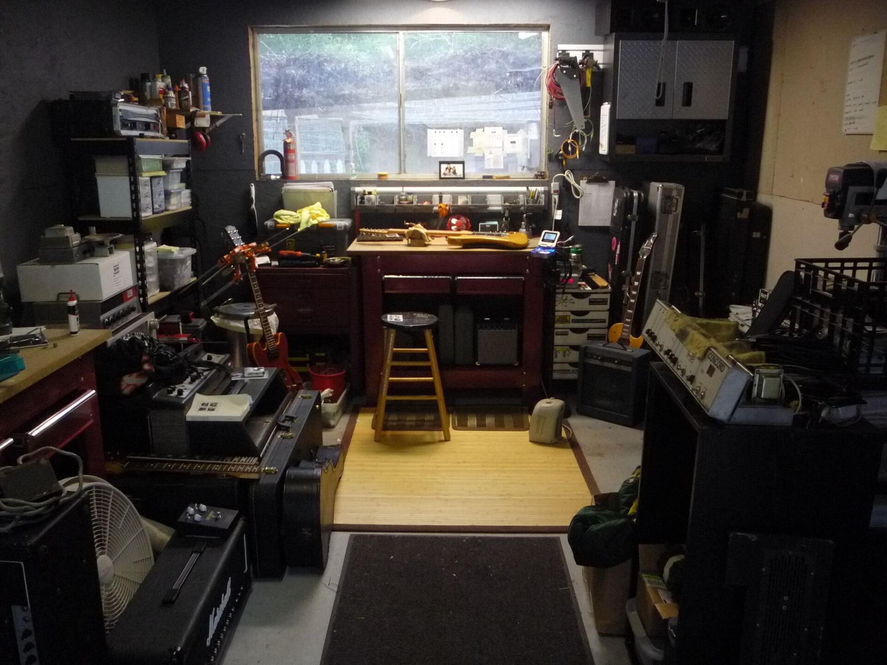 A cluttered, well-used instrument repair workshop with amplifiers and a workbench