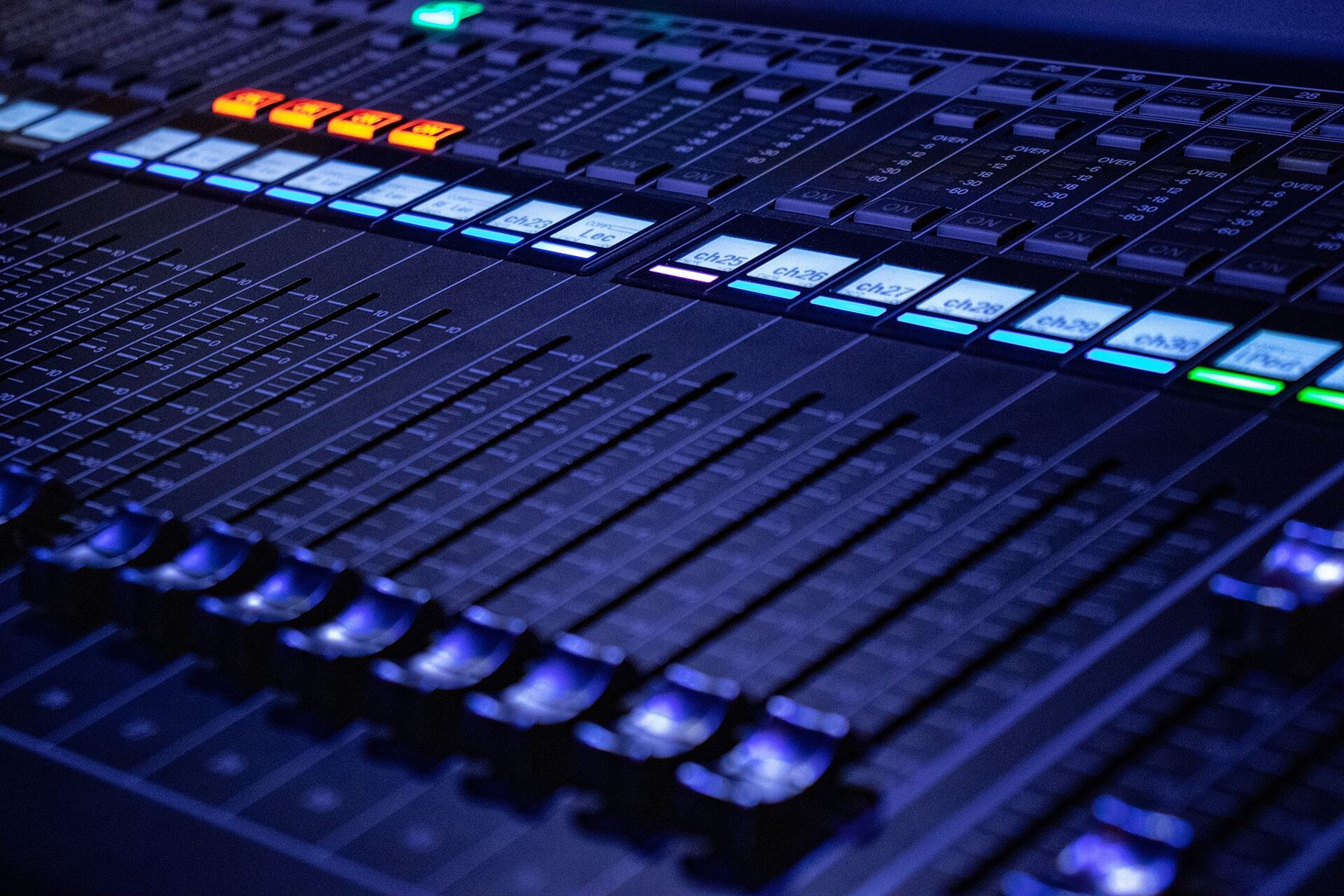 A large digital mixing console glowing with blue light in a dark studio