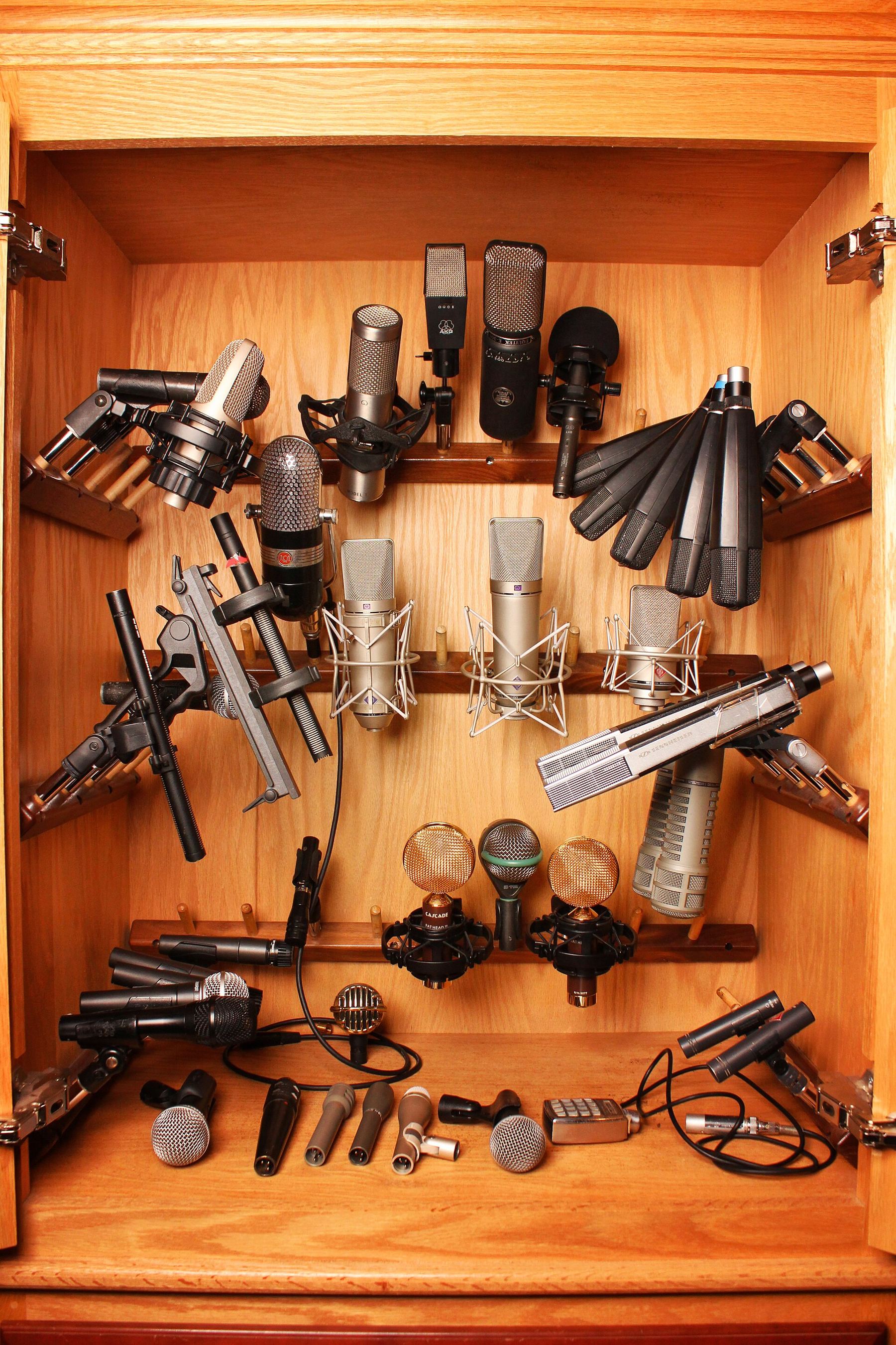 A wooden cabinet holding a collection of studio microphones