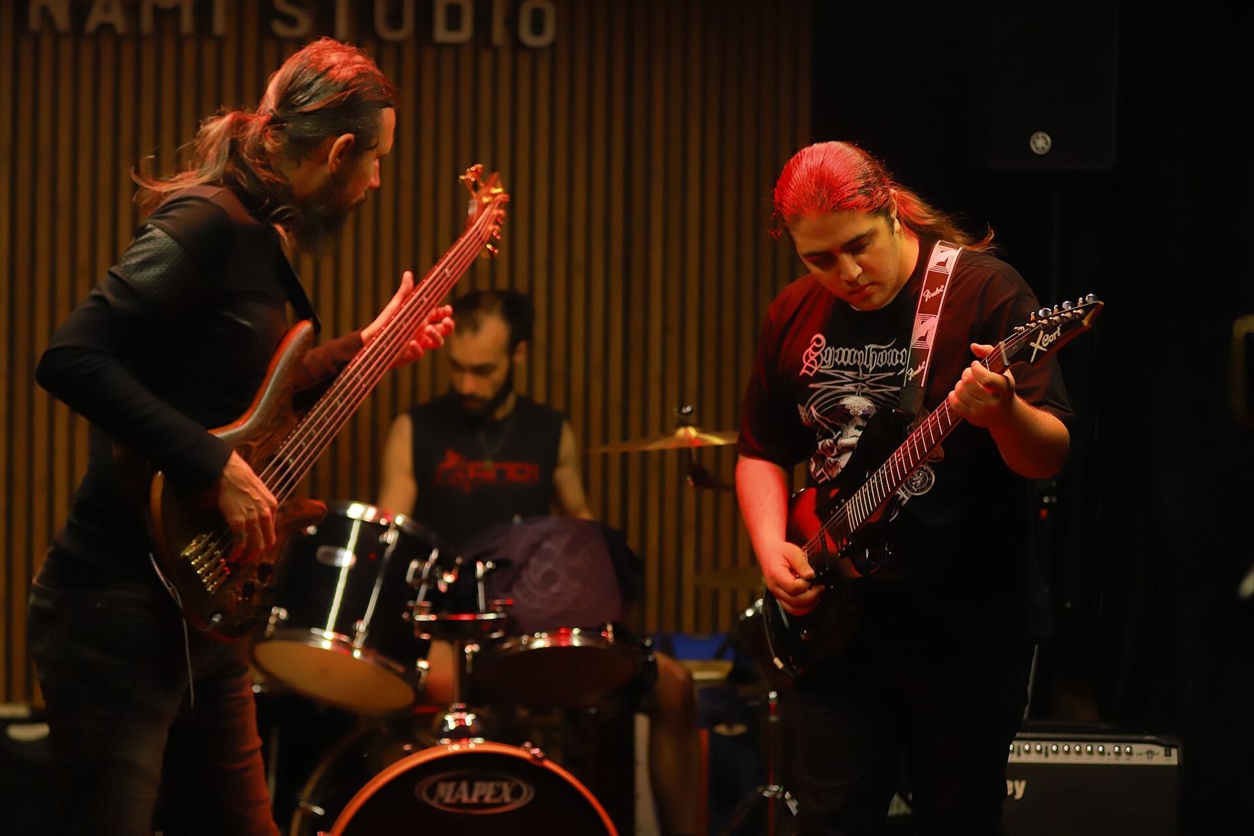 A band rehearsing with bass, guitar and drums in a warm-lit studio